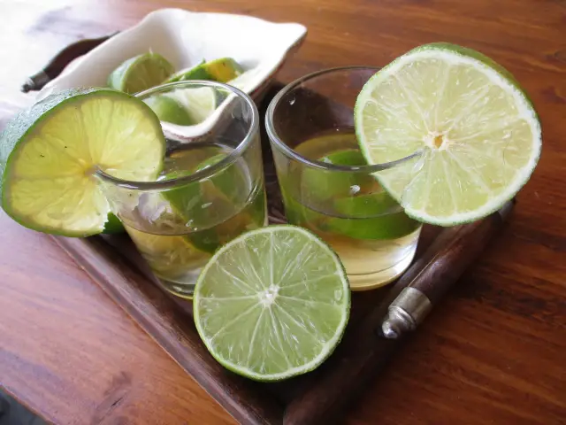 Deux ti-punchs servis avec des citrons verts sur un plateau en bois