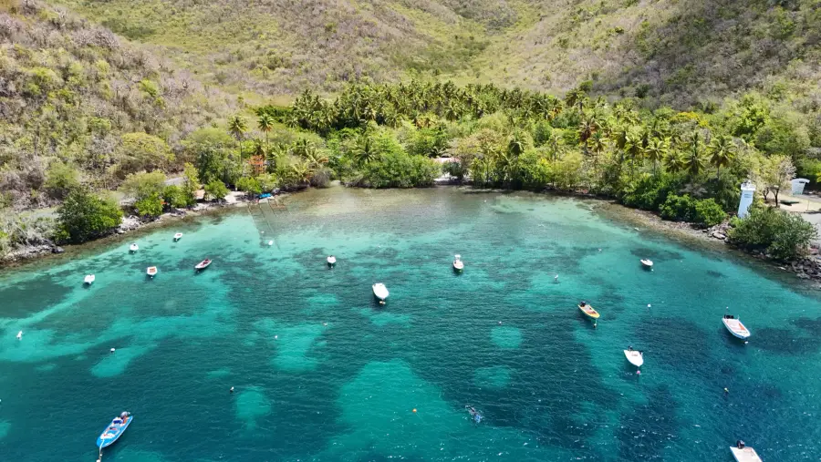 Anse aux eaux turquoise, bateaux au mouillage et phare, vue de drone